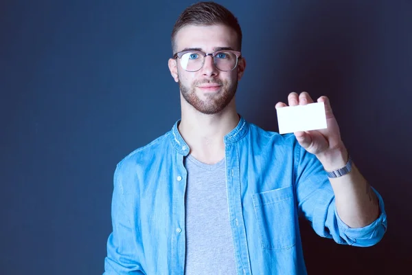 Joven sosteniendo una tarjeta de crédito de pie sobre fondo gris. Joven empresario. —  Fotos de Stock