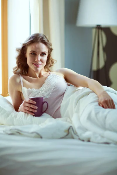 Junge Frau trinkt Kaffee oder Tee im Bett. — Stockfoto