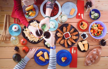 Ahşap masada otururken birlikte yemek yiyen bir grup insanın üst düzey görüntüsü. Masada yemek var. İnsanlar fast food yiyor..