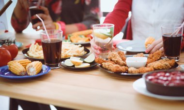 Ahşap masada otururken birlikte yemek yiyen bir grup insanın üst düzey görüntüsü. Masada yemek var. İnsanlar fast food yiyor..