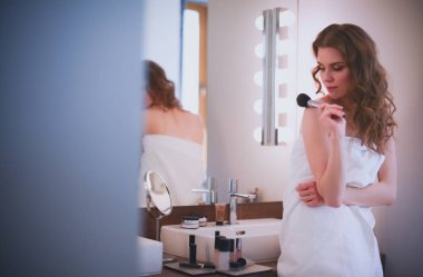 Genç bir kadın aynaya bakıyor ve makyaj yapıyor..