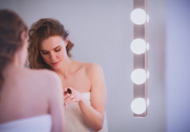 Genç bir kadın aynaya bakıyor ve makyaj yapıyor..