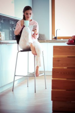 modern mutfakta otururken cep telefonu kullanan kadın.
