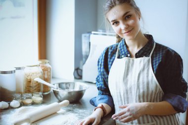 Güzel bir kadın mutfakta pasta pişiriyor. Masanın yanında duruyor..