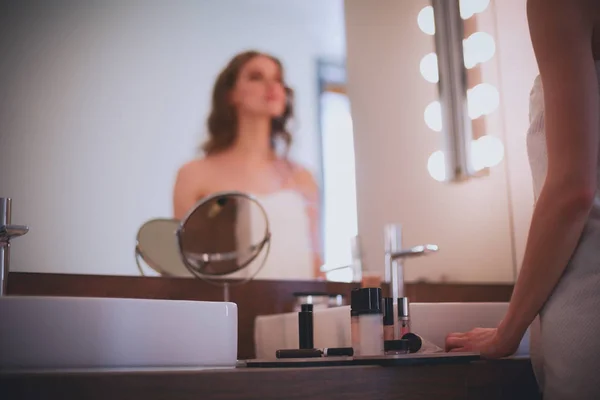 Mujer joven mirándose en el espejo y maquillándose. — Foto de Stock