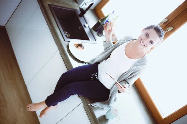 Krásná mladá žena pomocí digitální tablet v kuchyni. — Stock fotografie