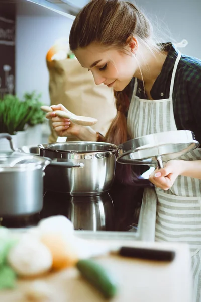 Jeune femme debout près de la cuisinière dans la cuisine . — Photo