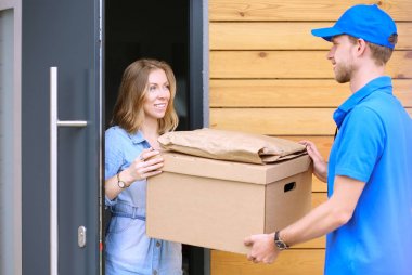 Mavi üniformalı gülümseyen kurye servis konseptine paket kutusu teslim eden teslimatçı. Mavi üniformalı gülümseyen teslimatçı.