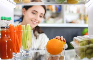 Sağlıklı yiyecek, sebze ve meyvelerle dolu açık buzdolabının yanında duran kadın portresi. Kadın portresi