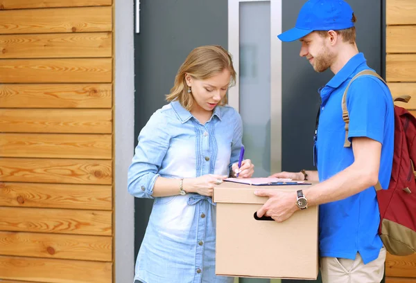 Repartidor sonriente con uniforme azul que entrega la caja de paquetes al destinatario: concepto de servicio de mensajería. Repartidor sonriente en uniforme azul — Foto de Stock