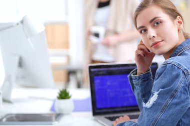 İki genç kadın masada enstrümanlar, planlar ve dizüstü bilgisayarlarla oturuyor..