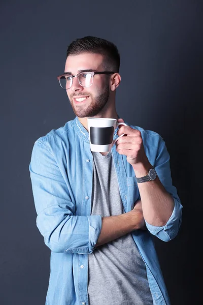 Portret przystojny, młody człowiek, stojąc i trzymając kubek kawy w rękach — Zdjęcie stockowe