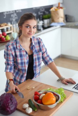 Masanın yanındaki mutfakta sebze doğrayan genç bir kadın..