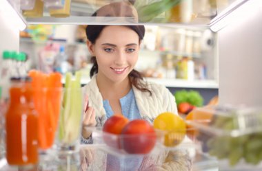 Sağlıklı yiyecek, sebze ve meyvelerle dolu açık buzdolabının yanında duran kadın portresi. Kadın portresi