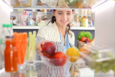 Sağlıklı yiyecek, sebze ve meyvelerle dolu açık buzdolabının yanında duran kadın portresi. Kadın portresi