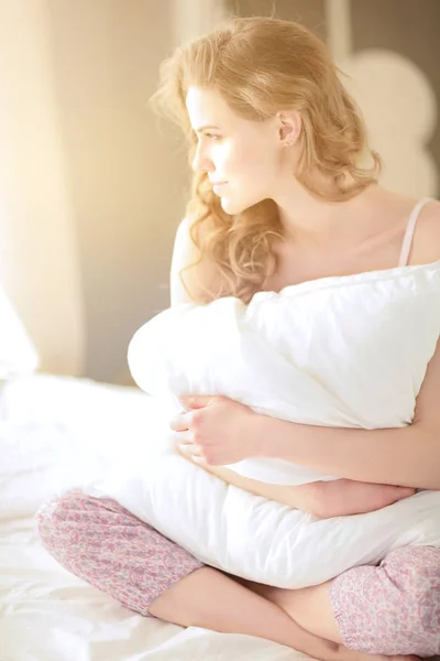 Young woman holding a pillow while sitting on her bed. — Stock Photo, Image