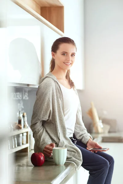 Kvinna med mobiltelefon sitter i moderna kök. — Stockfoto