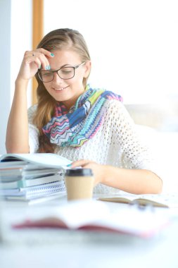 Kitapların arasında bir masada oturan genç bir kadın. Öğrenci