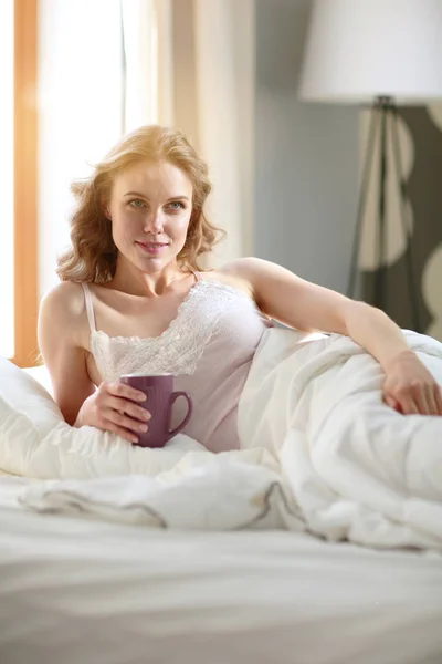 Young woman drinking cup of coffee or tea while lying in bed. — Stock Photo, Image