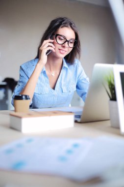 Ofis masasında oturan ve cep telefonuyla konuşan genç ve güzel bir iş kadını. İş kadını