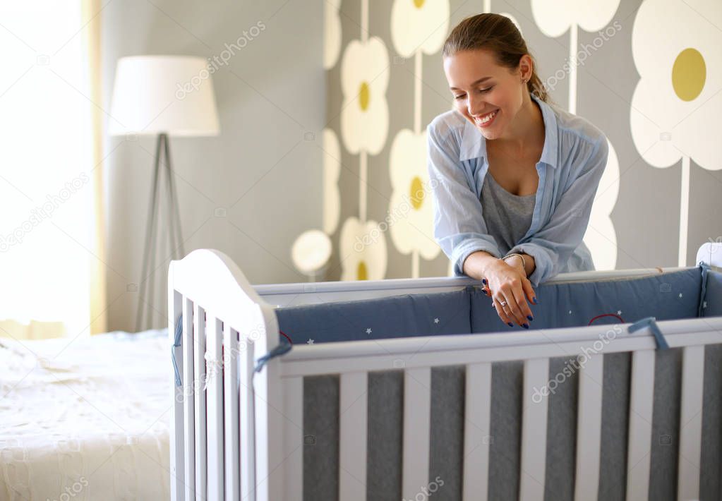 Young woman standing near childrens cot. Young mom
