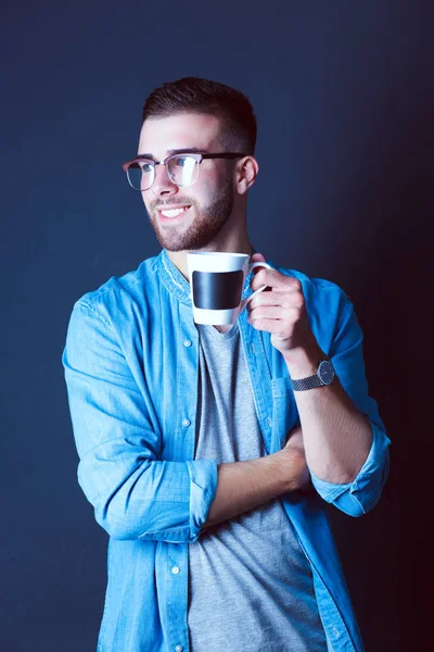 Portret van een knappe jongeman permanent en houden van een kopje koffie in zijn handen — Stockfoto