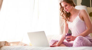 Dizüstü bilgisayar ile yatakta oturan genç güzel kadın