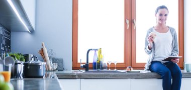 Mutfakta dijital tablet kullanan güzel genç bir kadın.