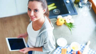 Tablette tarifi takip eden bir kadın evde yemek pişiriyor.