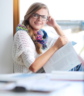 Kitapların arasında bir masada oturan genç bir kadın. Öğrenci