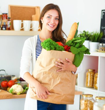 Elinde sebzeli alışveriş torbası tutan genç bir kadın.