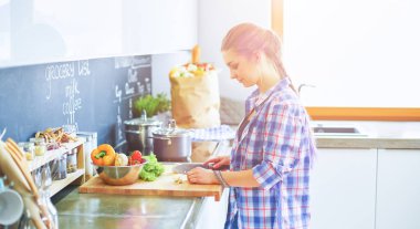 Masanın yanındaki mutfakta sebze doğrayan genç bir kadın.
