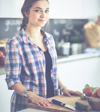 Masanın yanındaki mutfakta sebze doğrayan genç bir kadın.