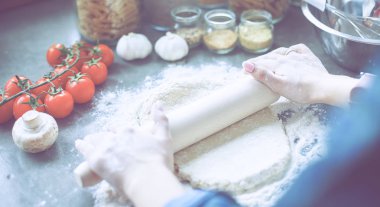 Güzel bir kadın mutfakta pasta pişiriyor. Masanın yanında duruyor.