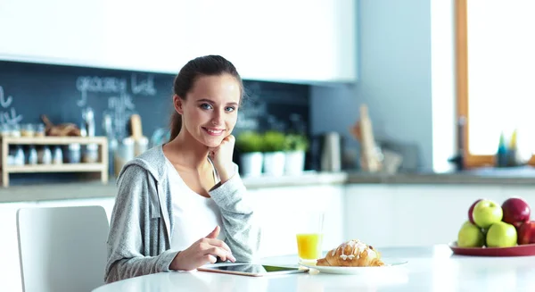 Mujer joven con jugo de naranja y tableta en la cocina —  Fotos de Stock