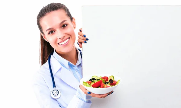 Портрет красивой женщины-врача, держащей тарелку со свежими овощами, стоящими рядом с пустым — стоковое фото