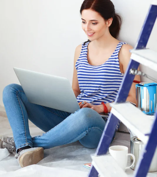 Retrato de mujer joven mientras pinta nuevo apartamento, sentado con el ordenador portátil — Foto de Stock