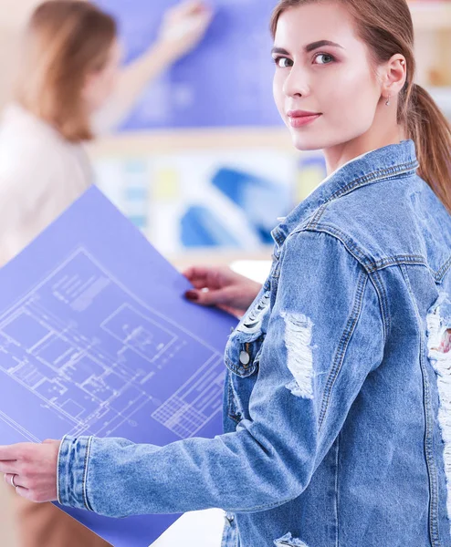 Twee jonge vrouw in de buurt van bureau met instrumenten, plan en laptop — Stockfoto