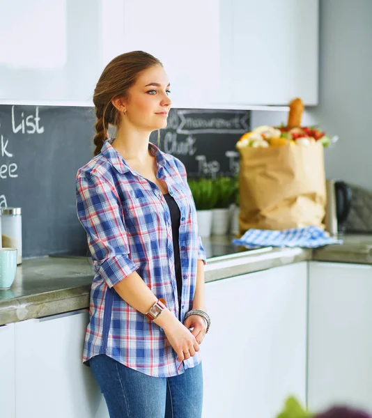 Portret młodej kobiety stojącej z rękami na tle kuchni — Zdjęcie stockowe