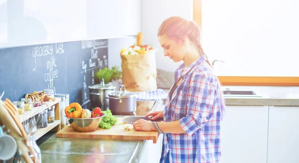 Młoda kobieta kroi warzywa w kuchni przy biurku — Zdjęcie stockowe