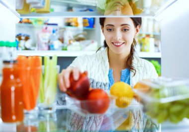 Sağlıklı yiyecek, sebze ve meyvelerle dolu açık buzdolabının yanında duran kadın portresi. Kadın portresi