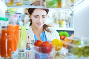Sağlıklı yiyecek, sebze ve meyvelerle dolu açık buzdolabının yanında duran kadın portresi. Kadın portresi