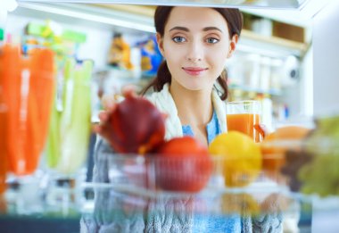 Sağlıklı yiyecek, sebze ve meyvelerle dolu açık buzdolabının yanında duran kadın portresi. Kadın portresi