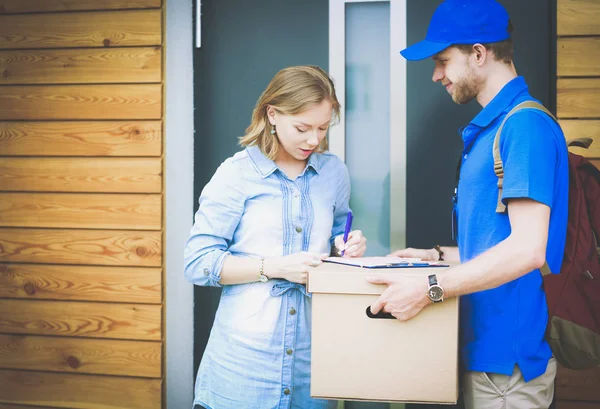 Repartidor sonriente con uniforme azul que entrega la caja de paquetes al destinatario: concepto de servicio de mensajería. Repartidor sonriente en uniforme azul — Foto de Stock