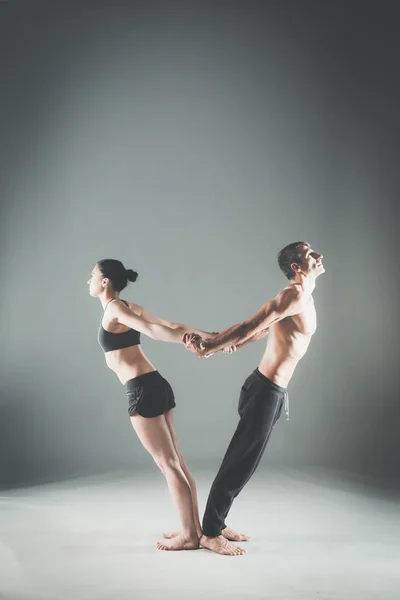 Casal jovem praticando acro ioga no tapete em estúdio juntos. Acroyoga. Um par de ioga. Parceiro ioga . — Fotografia de Stock