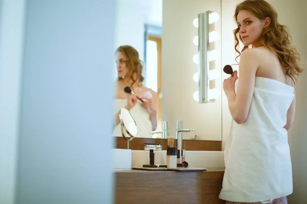 Young woman looking in the mirror and putting make-up on. — Stock Photo, Image