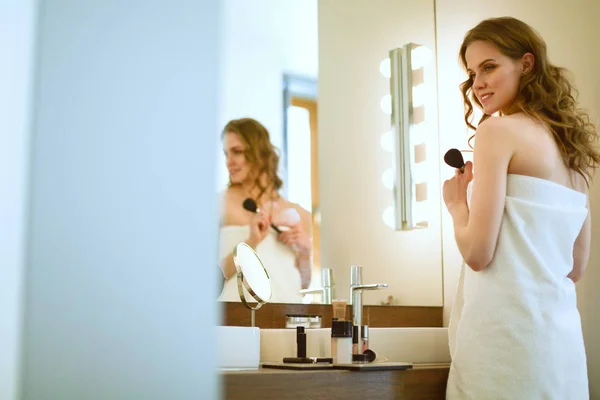 Jonge vrouw kijken in de spiegel en zetten make-up op. — Stockfoto