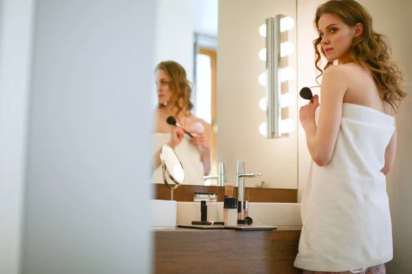 Mujer joven mirándose en el espejo y maquillándose. — Foto de Stock