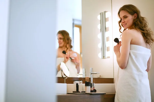 Молода жінка дивиться у дзеркало і одягає макіяж . — стокове фото