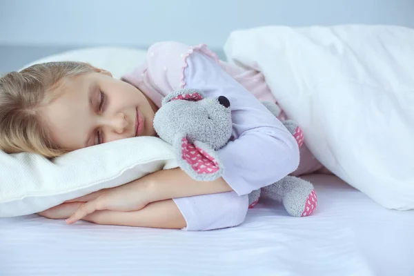 Kind meisje slaapt in het bed met een speeltje teddy beer — Stockfoto
